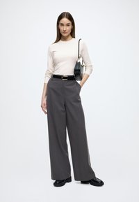 Beiges, geripptes Langarmoberteil kombiniert mit hoch taillierter, weitem grauem Hosenrock. Schwarzer Lackgürtel und Handtasche, klobige schwarze Schuhe, minimalistischer Stil.