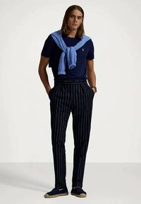 Tumši zils T-krekls, gaiši zils džemperis pār pleciem, tumši zili bikses ar smalkiem svītrējumiem, tumšas espadrilles, taisnas kājas dizains, brīvs piegriezums.