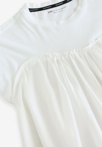 Hvid T-shirt med rund hals og en indsnøring i bunden. Lavet af blødt stof og har et sømløst design.