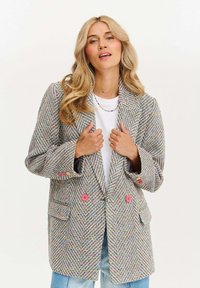 Sako s vzorem houndstooth v šedé barvě a multikolorových nitích, se dvěma růžovými knoflíky a dvěma předními kapsami; dvouřadý design.