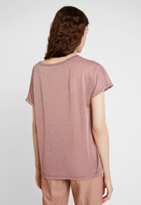 Rose gold, short-sleeve top with a shiny texture. Relaxed fit, rounded neckline, and a subtle shimmer. Hemline sits below the hips.