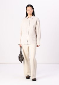 Light beige linen shirt with a button-down design, paired with off-white flared pants and a small brown handbag. Simple, minimalistic style.