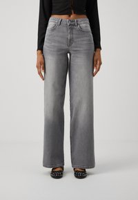 Šedé široké džíny s mid-rise pasem, pětimi páčkovým designem a bledým ombré. Stylizované s černými ozdobenými balerínami a cropped topem.