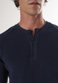 Granatowa, prążkowana, długozapinana koszula henley z okrągłym dekoltem, trzema guzikami i małym otworem przy górnym guziku.