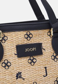 Sac en paille tressée avec des accents en cuir bleu marine, des motifs floraux brodés et un badge logo doré. Dispose de poignées robustes pour le transport.