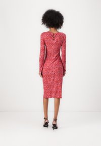 Langärmliges rotes Kleid mit Leopardenmuster, mit Schlüsselloch-Rücken, taillierter Passform und knieumspielendem Saum. Getragen mit schwarzen High Heels.