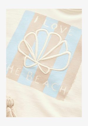 Fehér szövet, amely világoskék és bézs csíkos mintával rendelkezik, egy hímzett kagylóval és a "IMÁDOM A TENGERPARTOT" felirattal fehér színben.