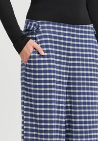 Karierte weit geschnittene Hose in Marineblau und Weiß, mit einer Tasche und einem eingezogenen Bund. Aus einem strukturierten, gewebten Stoff gefertigt.