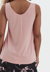 Top senza maniche di un rosa chiaro con scollo tondo. Tessuto morbido con una texture liscia, abbinato a una gonna nera con motivo floreale.