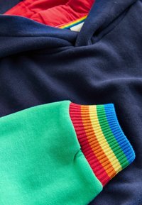 Granatowa bluza z kapturem z zielonym rękawem i wielokolorowymi ściągaczami w kolorach czerwonym, pomarańczowym, żółtym, niebieskim i zielonym. Gładka tekstura tkaniny.