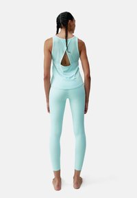 Een mintgroene sportieve tanktop en legging, met een uitsnijdetail op de rug. De stof lijkt glad en aansluitend.