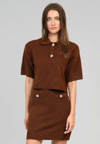 Ensemble en tricot marron composé de deux pièces, avec un col polo, des manches courtes et des boutons décoratifs sur les poches de la jupe. Texture douce, bords côtelés.