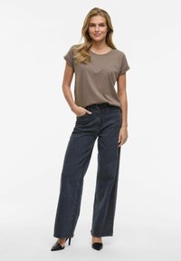 Camiseta corta de manga corta color marrón combinada con unos pantalones vaqueros de pierna ancha de denim oscuro de cintura alta y tacones negros de punta. Tejido suave y corte relajado.