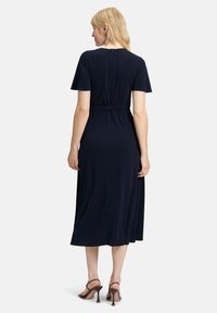 Robe midi bleu marine avec des manches courtes, une taille élastique et un col rond. Le tissu est lisse, avec un détail de fermeture éclair dans le dos.