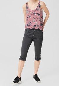 Débardeur floral rose avec un col rond, associé à un pantalon cropped gris foncé avec une fermeture à boutons et des ourlets retroussés, porté avec des baskets noires.