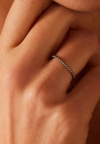 Zilveren ring met een parelachtige textuur, licht reflecterende afwerking, gedragen op een hand met een zachte huid, die de ronde vorm en het design benadrukt.