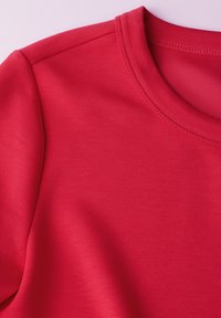 Czerwona koszulka z krótkim rękawem i okrągłym dekoltem. Wykonana z gładkiego, elastycznego materiału z widocznymi szwami wzdłuż kołnierza i szwów ramion.