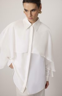 Hvid bluse med struktureret krave, lagdelt design og gennemsigtig stofoverlæsning. Har en knaplukning og flagrende ærmer.