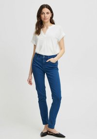 Valge lühikese varrukaga T-särk V-kaelusega, kombineeritud siniste kitsaste teksadega. Mustad lapsed kingad täiustavad komplekti. Lihtne, puhas disain ilma mustriteta.