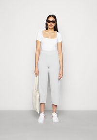 Top branco de decote quadrado, calças largas cinzas e sapatilhas brancas com detalhes laranja. Modelo segura uma mala tote bege, usando óculos de sol escuros.