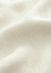 Tessuto beige chiaro con una trama testurizzata, che mostra un aspetto morbido e liscio. Sutili variazioni di colore creano un aspetto naturale.