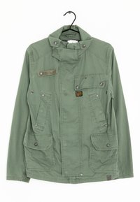 Olivově zelená bunda vyrobená z texturované tkaniny, se stojáčkem, několika předními kapsami a akcenty na patentky.