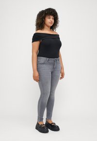 Fekete, váll nélküli bodysuit, szürke, skinny farmer zsebekkel és fekete, csatos részletekkel ellátott platform cipők. Göndör haj.