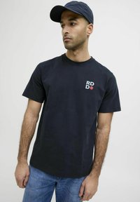 Marineblå bomulds t-shirt med korte ærmer og rund halsudskæring. Har hvid og rød trykt tekst på venstre brystområde.