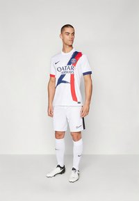 Bela nogometna oprema z modrimi in rdečimi poudarki, diagonalen vzorec, sponzorjev logotip in blagovna znamka Nike. Kratki rokavi, kombinirana s kratkimi hlačami in nogometnimi čevlji.