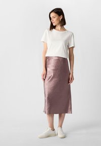 Lekki, biały bawełniany T-shirt zestawiony z długą, miękką, pogniecioną spódnicą z satyny w kolorze różowego złota i białymi trampkami. Prosty, minimalistyczny design.