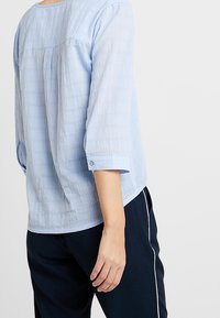 Hellbluse mit Struktur, dreiviertelärmeln, rundem Ausschnitt und geknöpften Manschetten. Mit einer Passe und Falten-Details auf der Rückseite gestaltet.