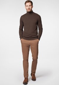 Brązowy sweter typu golf, dopasowany krój, prążkowane mankiety. Beżowe spodnie slim fit, gładka faktura. Brązowe zamszowe buty sznurowane, casualowy styl.