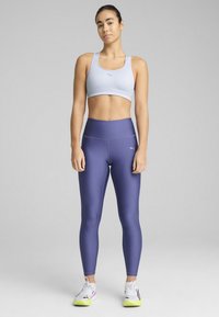 Lysblå sports-bh og mørk lilla højtaljede leggings, lavet af glat materiale. Sneakers har hvide og neongule detaljer.