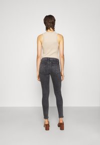 Jeans ajustados de denim gris oscuro con un lavado sutil, combinados con una camiseta sin mangas texturizada beige clara y sandalias de tacón cuadrado marrones.