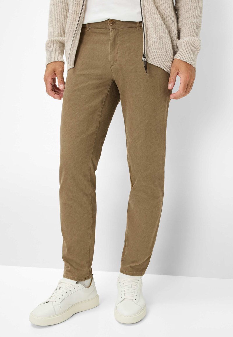 Slank gesneden bruine chinos gemaakt van een duurzaam materiaal, met een sluiting met knopen aan de voorkant, zijzakken, en gecombineerd met witte sneakers.
