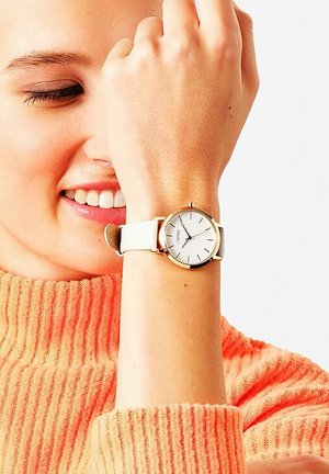 Weißer Uhr mit rundem Gehäuse aus goldfarbenem Metall und weißem Ziffernblatt, ausgestattet mit goldenen Stundenmarkierungen und einem weißen Lederarmband, getragen am Handgelenk.