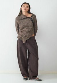 Bruine gestructureerde trui met een ritskraag, gecombineerd met hoge, donkere bruin, wijde broekspijpen. Zwarte ballerina's maken de look compleet.