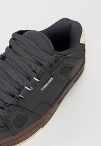Szürke skate cipők párnázott hálós nyelvvel, vastag szürke fűzőkkel, texturált szintetikus felső résszel és barna gumitalppal, melyen a "GLOBE" logó található.