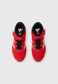 Red athletic shoes with mesh material, black accents, white sole, and grey stripes, featuring a Velcro strap and laces for secure fit.