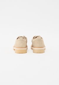 Chaussures en daim beige avec une forme arrondie, semelle plate en caoutchouc et tirette. Présentent des coutures minimales et des lignes épurées avec un design confortable.