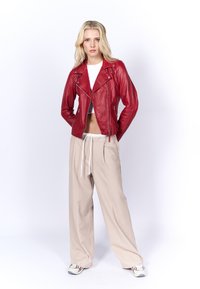 Rode leren cropped motorjack met zilveren hardware, gecombineerd met beige wijde broek met een trekkoord in de taille.