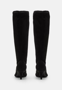 Paar schwarze kniehohe Stiefel aus Wildleder mit schlanken Abs ätzen, von hinten vor weißem Hintergrund gezeigt.