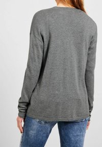 Grå, långärmad tröja med avslappnad passform, ribbade muddar och nederkant, samt en slät textur. Bärs med ljusblå jeans.