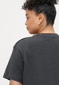 Koszulka w kolorze węgla o krótkich rękawach, z teksturowanej tkaniny, okrągłym dekoltem i akcentami na ramionach. Mały detal z logo blisko rękawa.
