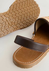 Sandale à bride en cuir marron avec semelle beige présentant un motif antidérapant texturé et des coutures blanches le long du bord.