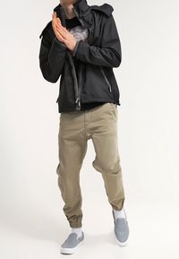 Czarna kurtka na zamek z wysokim kołnierzem, zestawiona z beżowymi, zwężanymi spodniami oraz szarymi butami wsuwanymi. Kurtka posiada dwie boczne kieszenie i gładką fakturę.