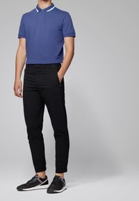 Polo blu con colletto a contrasto, pantaloni neri aderenti e sneaker nere. Il materiale appare liscio e traspirante.