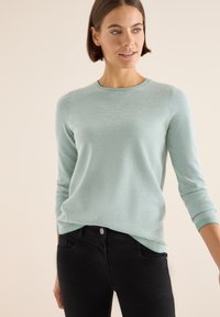 Hellblauer, strukturierter Pullover mit rundem Ausschnitt und Dreiviertelärmeln, kombiniert mit schwarzen Jeans. Besitzt eine lockere Passform.