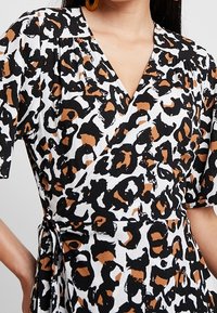Leopardmönstrad omlottklänning i vitt, svart och brunt. Korta ärmar, v-ringning och knytning vid midjan. Lättviktsmaterial med mjuk textur.