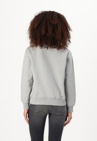 Felpa grigia con colletto rotondo, polsini e orlo a coste, texture morbida e vestibilità rilassata, mostrata di spalle con jeans scuri.